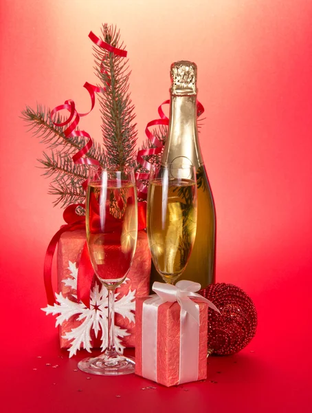 Sektflasche, Weingläser, Geschenke, Tannenzweig mit Lametta auf rotem Hintergrund — Stockfoto