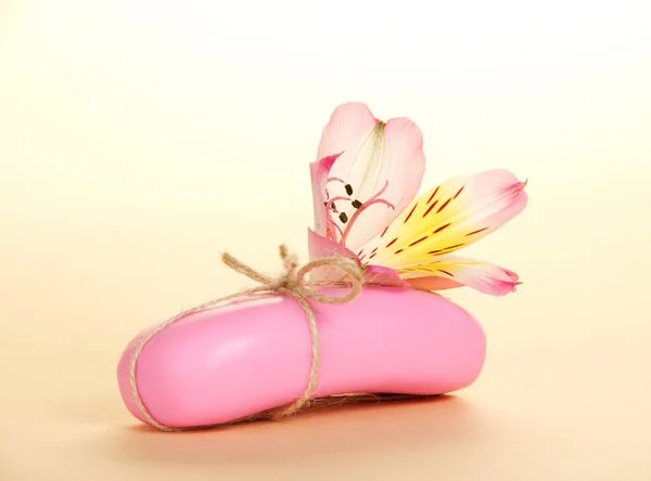 Кусок нового мыла, прикреплённого бечевкой и цветком на бежевом фоне — стоковое фото