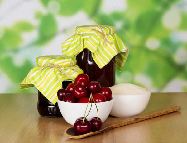 Vasi di marmellata, tazza di zucchero, cucchiaio di legno con ciliegie, bacche in una tazza su un tavolo — Foto Stock