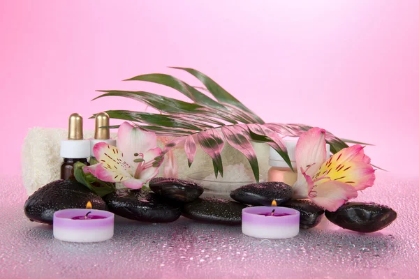 Foglia verde di un howea su sale, olio, pietre, candele e un asciugamano su uno sfondo rosa — Foto Stock