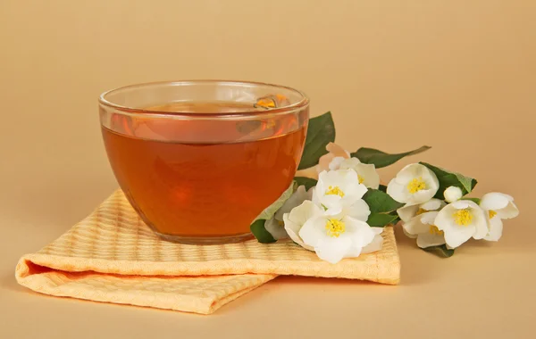 Cup of tea a branch of a jasmine and a napkin on a beige background — Stock Photo, Image