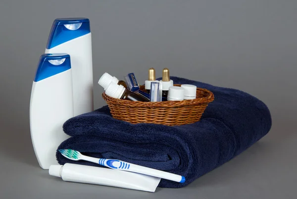 Shampoo, gel, cosmetics set in a braided basket, a towel on a grey background — Stock Photo, Image