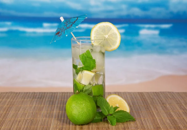 Mojito, a juicy lime, a lemon slice, on a bamboo cloth against the sea — Stock Photo, Image