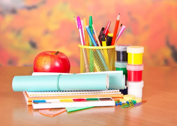 Writing materials, paints and an apple, on a table — Stock Photo, Image