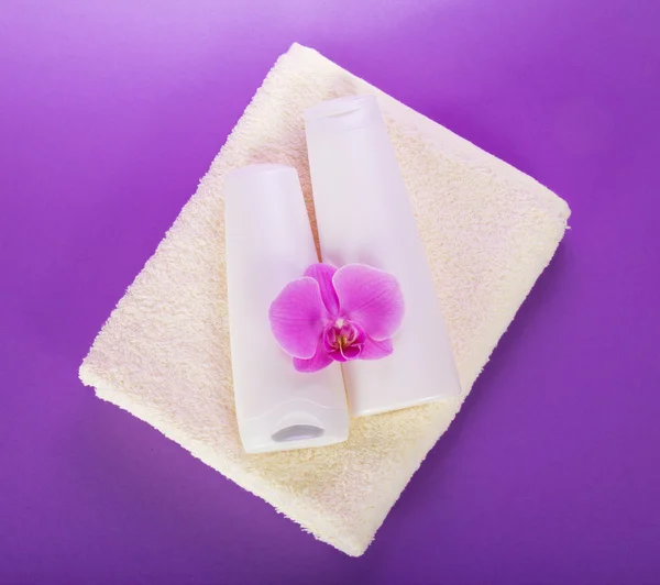 Shampoo en balsem conditioner op een terry handdoek, met een orchideebloem — Stockfoto
