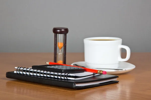 Notepad a pencil the calculator, cup of coffee, saucer, spoon and hourglasses — Stock Photo, Image