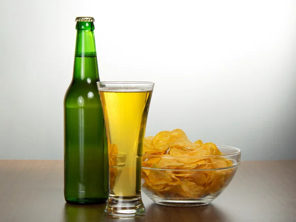 Bouteille de bière, bol avec des chips et un verre humide — Photo