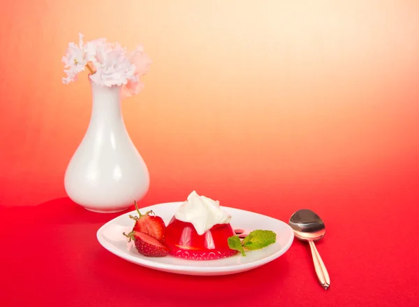Flowers in a vase, a plate with jelly and cream, a spoon — Stock Photo, Image