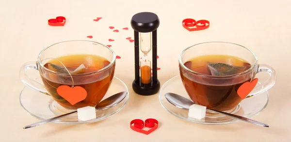 Two hot teas and hourglasses on a cloth decorated with hearts — Stock Photo, Image