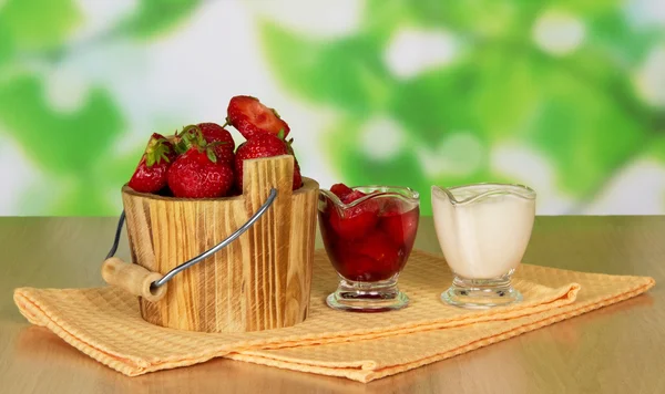 Fraise dans un seau dans une tasse une serviette et une tasse avec de la crème sur une table — Photo