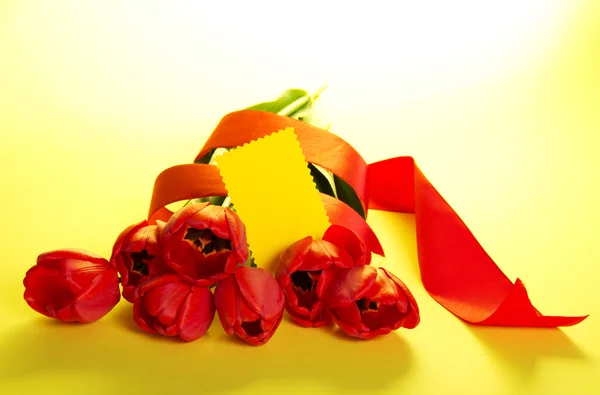 Il bouquet di tulipani decorato con un nastro e un biglietto vuoto per il testo su sfondo giallo — Foto Stock