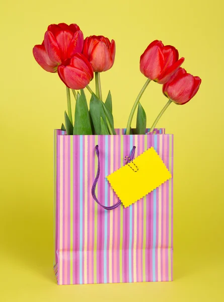 Buquê de tulipas em um pacote de presente e um cartão vazio em um fundo amarelo — Fotografia de Stock