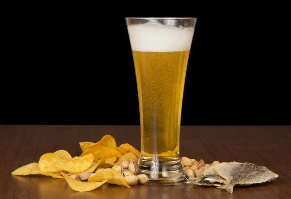 Glass of foamy beer with bubbles, chips, salty fish and the pistachios on the table — Stock Photo, Image