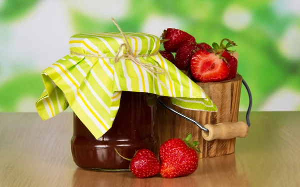 Bank with jam, a bucket with strawberry and a berries near, on a table — Stock Photo, Image