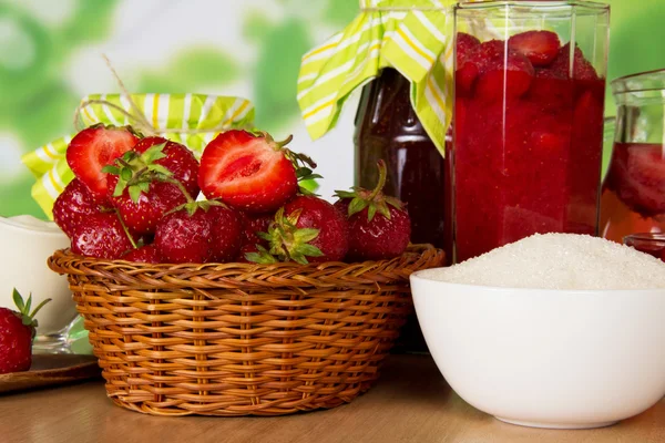 Sklenice džemu, koš s jahodovou, skla s plody a pohár s cukrem, closeup, na stůl — Stock fotografie