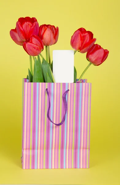 Букет тюльпанов в подарочном пакете и пустая карточка на желтом фоне — стоковое фото