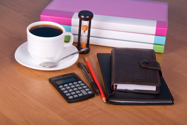 Notepad, organizer, pencil and pen, folders for documents the calculator, hourglasses and a cup of coffee on a table