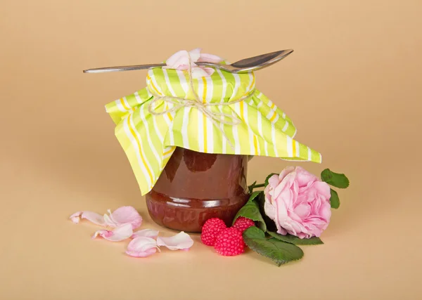 Glazen pot met frambozenjam, roze bloem op een beige achtergrond — Stockfoto