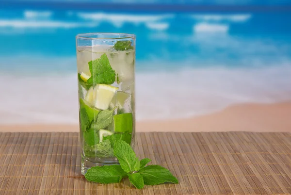 Green alcoholic cocktail from a citrus and mint, on a bamboo cloth against the sea