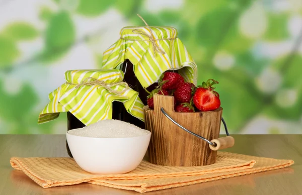 Pots de confiture, seau à la fraise une tasse avec du sucre et une serviette sur une table — Photo