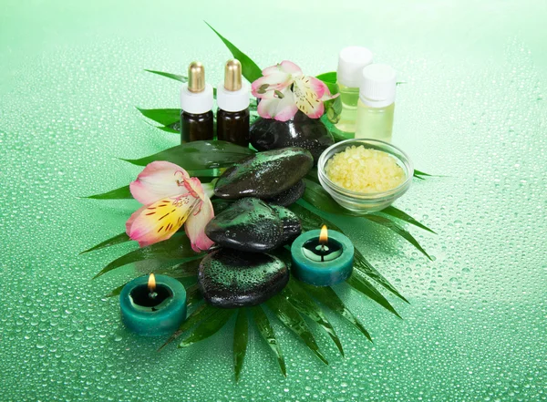 Velas e óleo de aroma, sal, pedras e uma flor em uma folha howea, em um contexto verde — Fotografia de Stock