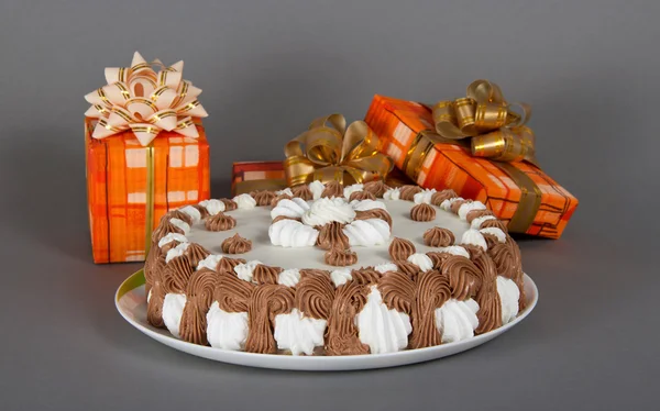 Il piatto con una torta e è un sacco di scatole regalo luminose sul grigio — Foto Stock