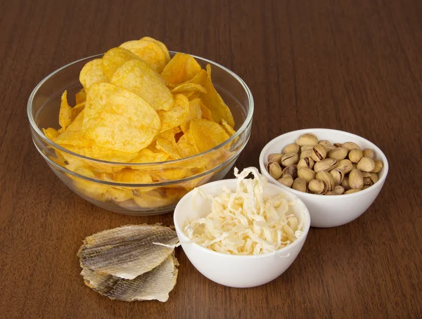 Chips, pistachios, dried squids and salty fish, on a table — Stock Photo, Image