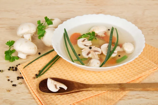 Plaat met soep, een houten lepel, veld champignons, peterselie en kruiden op een beige achtergrond — Stockfoto