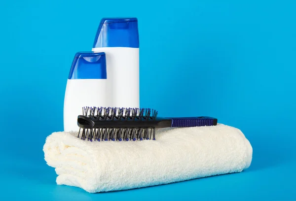 Cepillo de pelo sobre una toalla esponjosa, champú y gel sobre un fondo azul — Foto de Stock