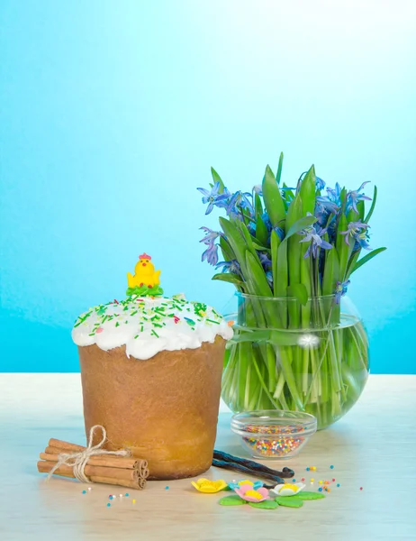 Pasen taart, zoete sieraden, kaneel, vanille, vaas met de bloemen op een tafel, op een blauwe achtergrond — Stockfoto