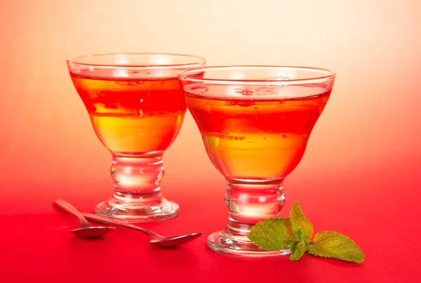 Two glasses of the fruit jelly, two teaspoons, spearmint leaf on a pink background — Stock Photo, Image