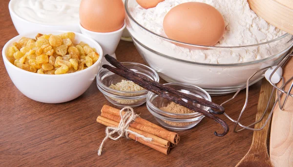 Russin, sesamfrö, pinnar kanel och vanilj baljor, ett mjöl, gräddfil och ägg på ett bord — Stockfoto