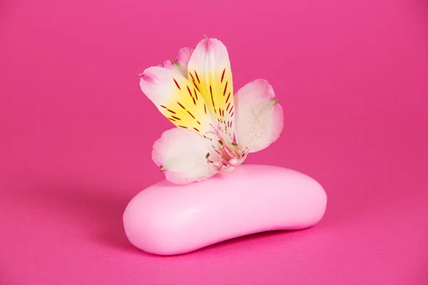 Кусок нового мыла и цветок на розовом фоне — стоковое фото