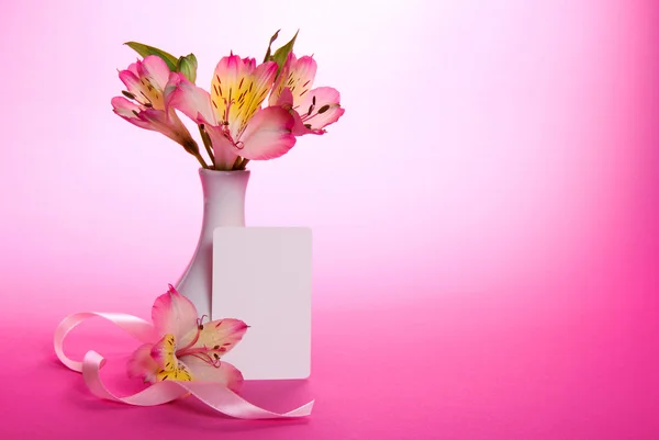 Розовая альстромерия в вазе и пустая открытка с лентой на розовом фоне — стоковое фото