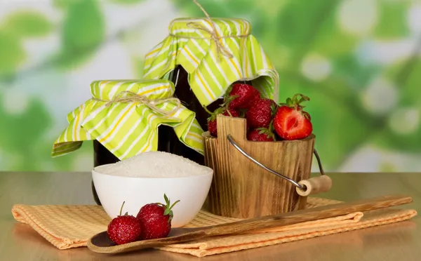 Jars of jam, bucket with strawberry a cup with sugar and a spoon with berries, napkins on a table — Stock Photo, Image