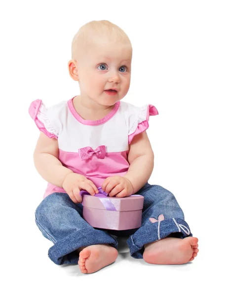 Das hübsche kleine Mädchen in rosa Jacke und blauer Jeans mit rosa Geschenkschachtel in Herzform. isoliert auf weiß — Stockfoto