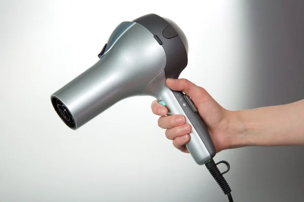 O secador de cabelo em uma mão em um contexto cinza — Fotografia de Stock