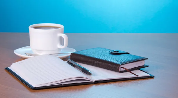 Open Kladblok de greep een organisator van een kopje koffie een schotel en een lepel op een tafel — Stockfoto