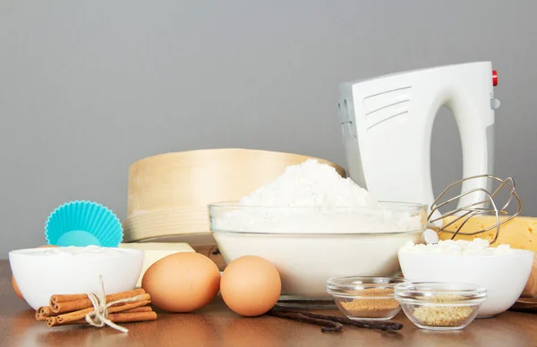 Meel, zuivelproducten, eieren, kruiden en mixer op een tafel, op een grijze achtergrond — Stockfoto