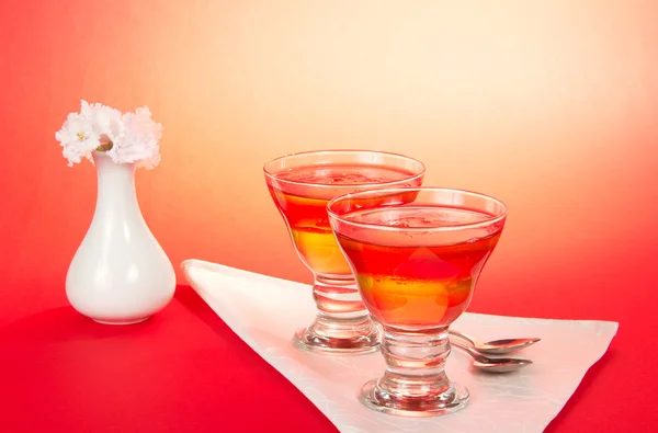 Dwie szklanki z galaretką i łyżki na serwetka, wazon z kwiatami na różowym tle — Zdjęcie stockowe