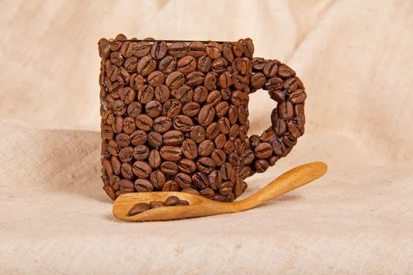 Coffee cup made from coffee beans, and wooden spoon, on a sackcloth — Stock Photo, Image