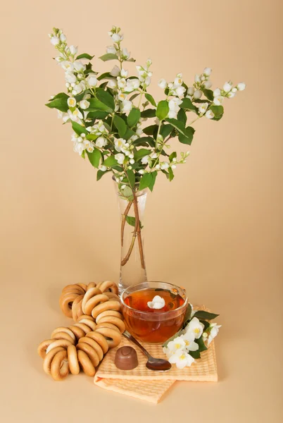 Cup of tea, bagels, chocolate and flowers in a vase on a beige background — Stock Photo, Image