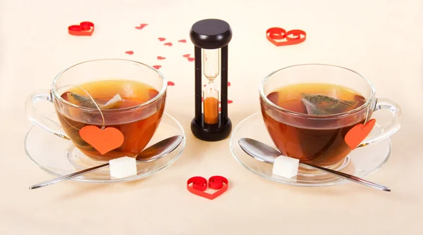 Two hot teas and hourglasses on a cloth decorated with hearts — Stock Photo, Image