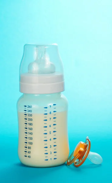 Μπουκάλι με γάλα και μια πιπίλα σε μπλε φόντο — Φωτογραφία Αρχείου