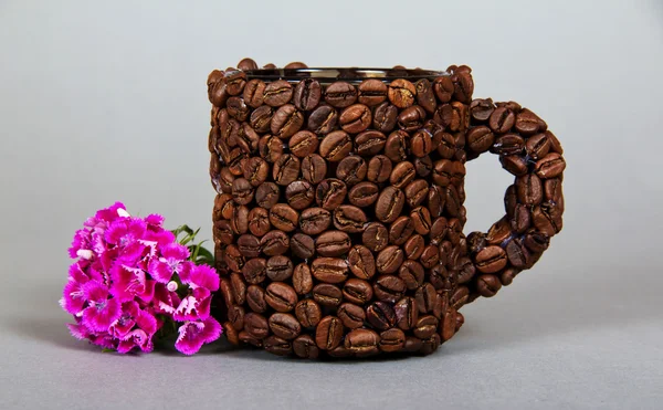 La tazza fatta di chicchi di caffè, un ramo di garofano luminoso su sfondo grigio — Foto Stock