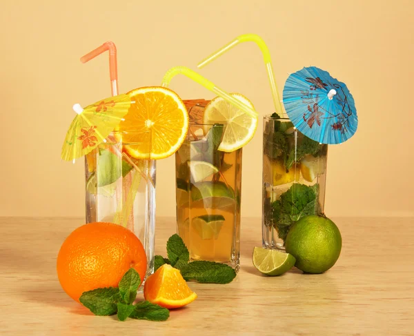Cocktail avec une paille et un parapluie, boisson avec une tranche d'orange, thé avec un citron, sur fond beige — Photo