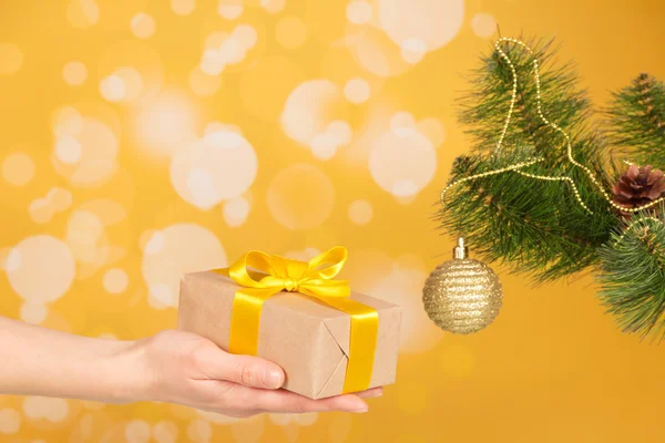 Ramo de abeto de Natal com ornamento e presente na mão — Fotografia de Stock