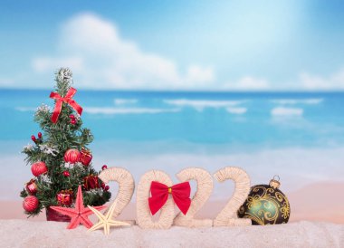 Noel konsepti. Yeni yıl tabelası, Noel ağacı ve plaj arka planında büyük bir top.