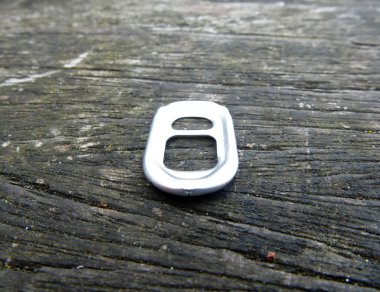 Aluminum pull tab laying on a wooden surface.