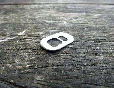 Aluminum pull tab laying on a wooden surface.